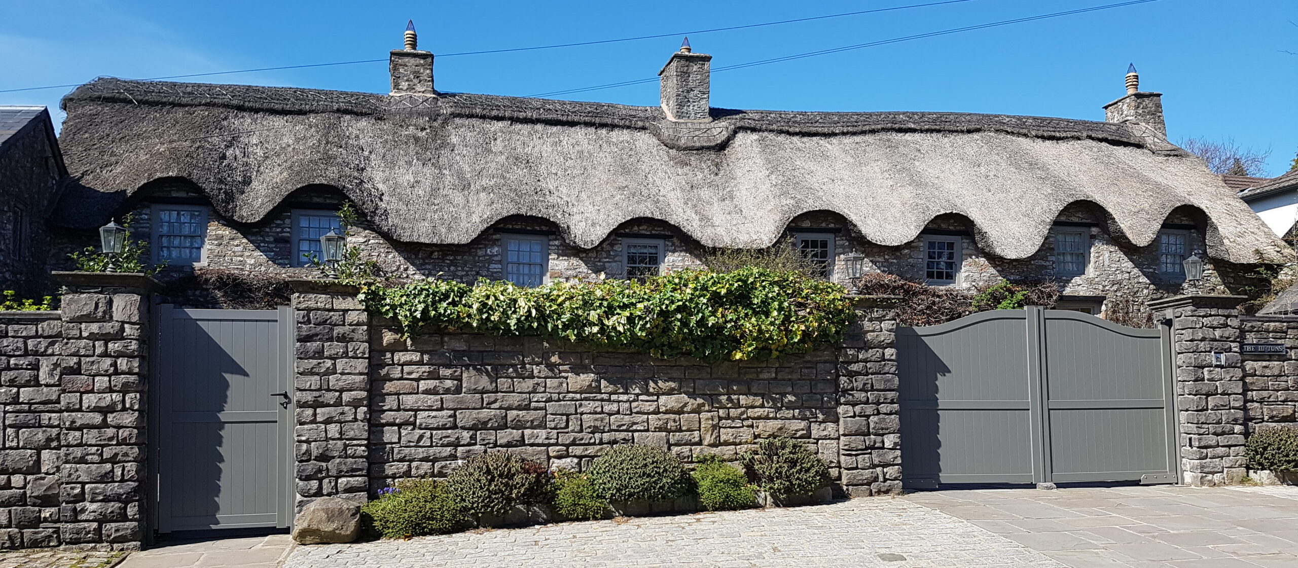 Large thatched house with a grey aluminium garden gate and a grey aluminium driveway gate