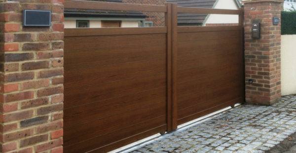 an brown Sliding aluminium driveway gate attached to two brick pillars