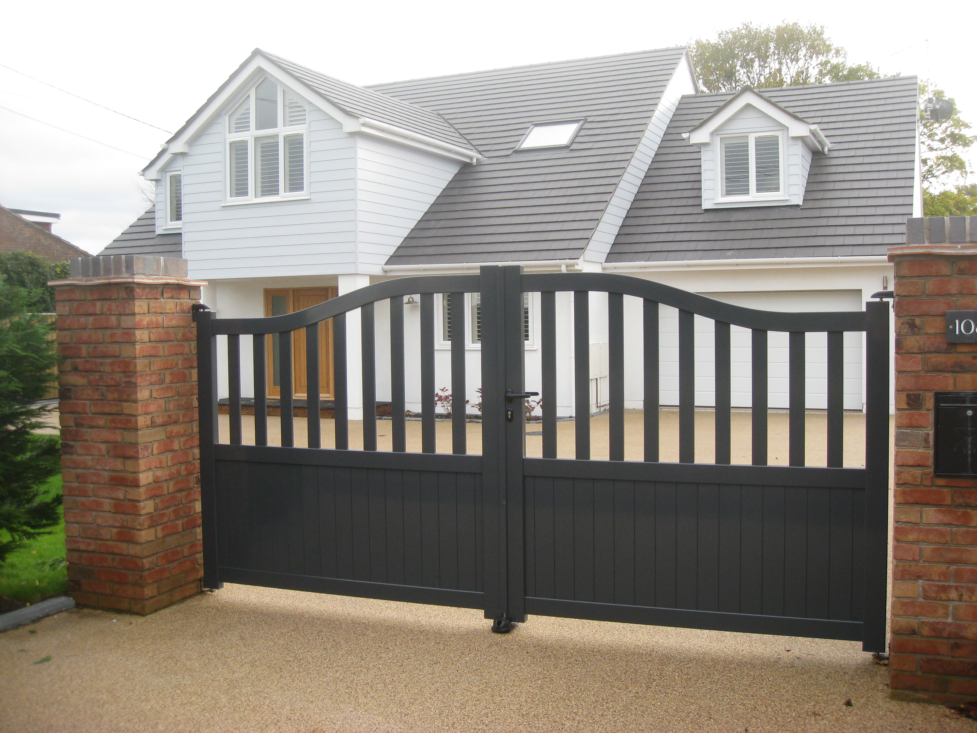 A charcoal finished aluminium driveway gate in front of a large white house